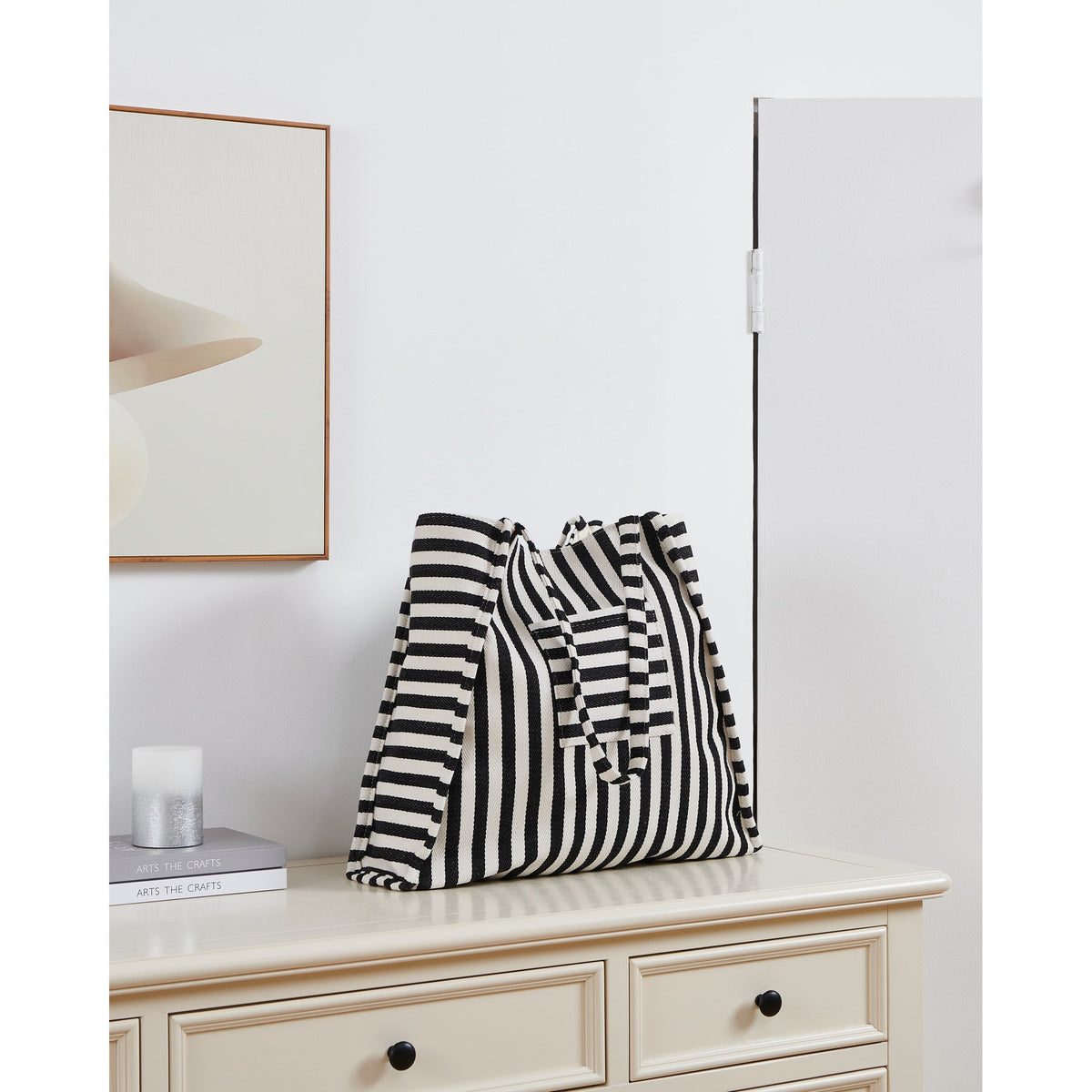 Bachuma Striped Bag in black and cream woven fabric with shoulder straps, shown on a cabinet in a room setting with framed art and a mirror.