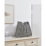 Bachuma Striped Bag in black and cream woven fabric with shoulder straps, shown on a cabinet in a room setting with framed art and a mirror.