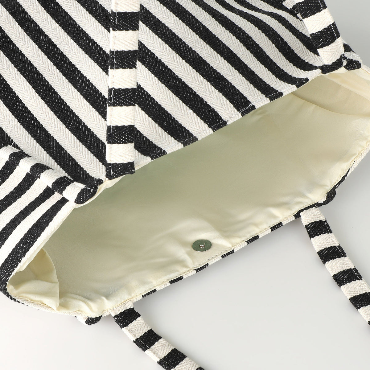 Close-up of the Bachuma Striped Bag in black and cream, showing the woven diagonal stripe fabric, striped shoulder straps, cream interior lining, and a snap fastening closure.