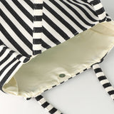 Close-up of the Bachuma Striped Bag in black and cream, showing the woven diagonal stripe fabric, striped shoulder straps, cream interior lining, and a snap fastening closure.