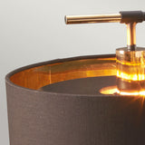 Close-up of the Balance Table Lamp - Brown/Polished Brass, showcasing a dark fabric shade and polished brass accents. The gold interior casts warm, energy-efficient lighting, while a sleek metallic horizontal handle elegantly contrasts with the soft texture of the shade.