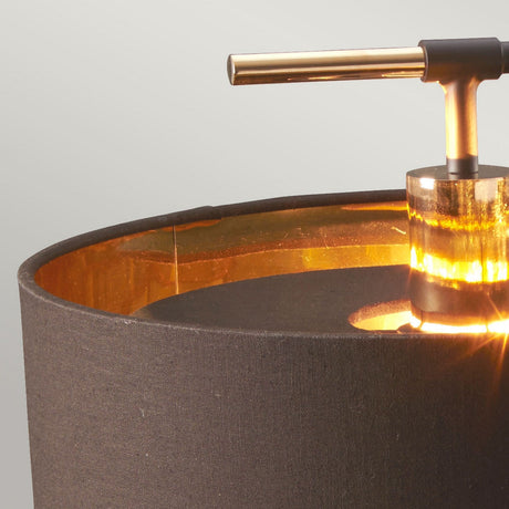 Close-up of the Balance Table Lamp - Brown/Polished Brass, showcasing a dark fabric shade and polished brass accents. The gold interior casts warm, energy-efficient lighting, while a sleek metallic horizontal handle elegantly contrasts with the soft texture of the shade.