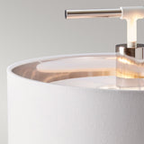 Close-up of the Balance 1 Light Table Lamp in polished nickel, featuring its top section with a cylindrical white fabric shade. The sleek metallic rod extends upward, offering a striking contrast against the smooth light grey background, epitomizing elegance and contemporary design.