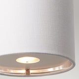 Close-up of the lit white fabric lampshade with a smooth texture from the Balance 1 Light Wall Light in Black/Polished Nickel. The energy-efficient bulb inside emits a soft, warm glow, set against a neutral gray background that highlights the simplicity and elegance of this modern wall light design.