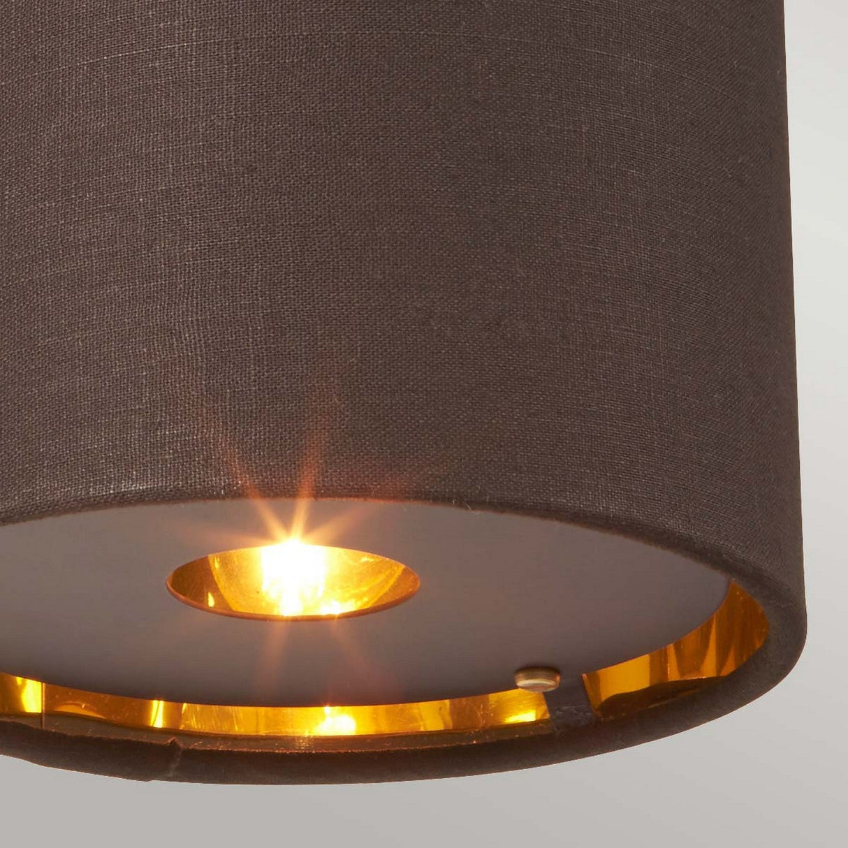 Close-up of the Balance 1 Light Wall Light, featuring a modern ceiling design with a dark brown fabric exterior and polished brass interior. Illuminated in Mid-Century Modern style, it casts a warm glow with visible light reflections inside the lampshade, echoing the elegance of polished brass.