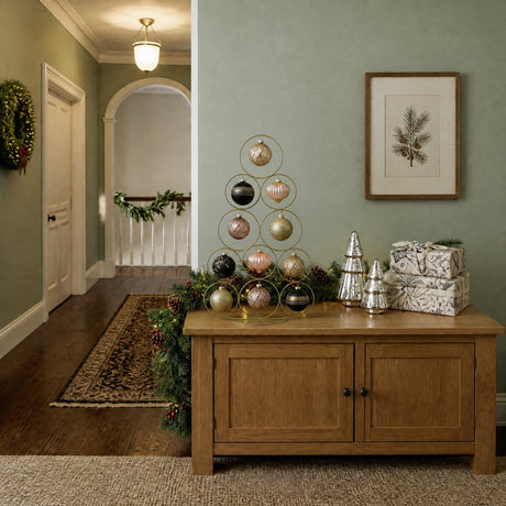 Ballymena 66cm metal Christmas tree in champagne finish, wire rings holding gold, pink and black baubles, displayed on a wooden sideboard in a festive hallway setting.
