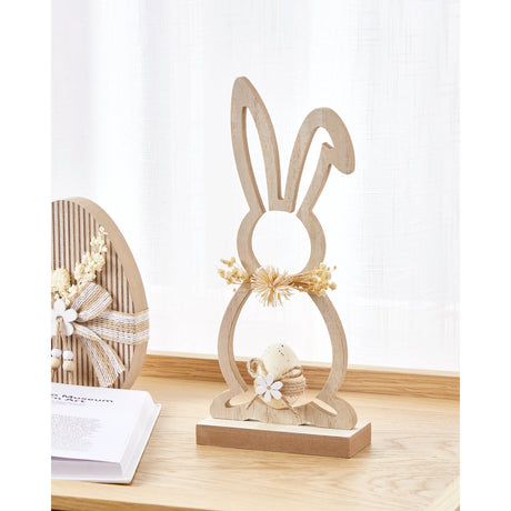 Balmaha wooden rabbit ornament with open cut-out outline, brown base, dried flower collar and speckled beige egg in a twine nest, shown on a shelf beside books.