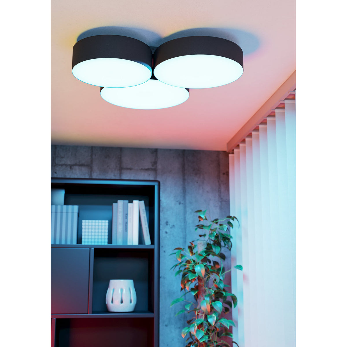 Barbano Smart LED flush ceiling light with three overlapping round drums in black fabric and white diffusers, shown glowing pink-toned in a living room above a dark bookshelf.