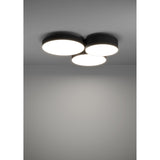 Barbano Smart LED flush ceiling light with three overlapping round drums in black fabric and steel with white diffusers, mounted on a grey ceiling illuminating the room below.