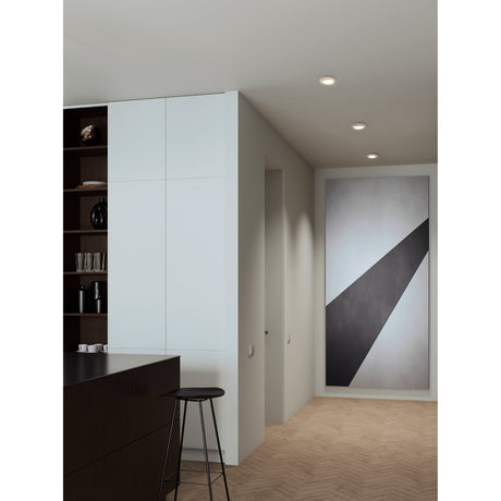 Barranco recessed downlights in white, round 9cm fittings installed in a hallway ceiling near a kitchen, shown alongside a dark bookshelf and framed wall art.