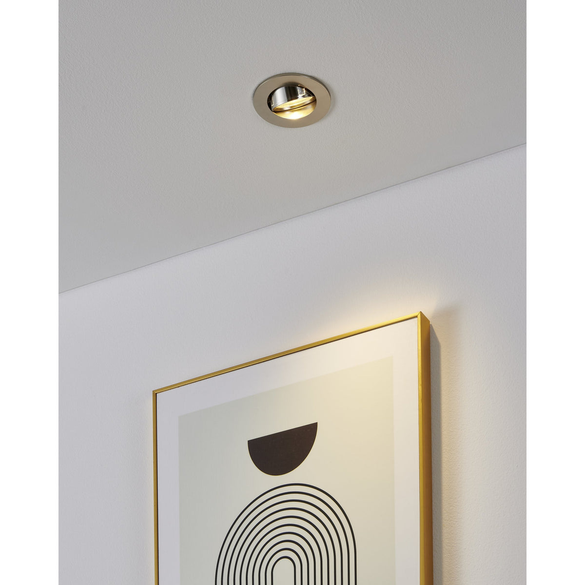 Barranco round recessed downlight in satin nickel with tiltable inner ring, shown on a white ceiling angled to highlight a framed print on the wall below.
