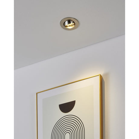 Barranco round recessed downlight in satin nickel with tiltable inner ring, shown on a white ceiling angled to highlight a framed print on the wall below.