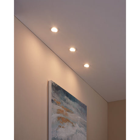 Baselle set of three round recessed downlights in white steel, installed in a hallway ceiling, casting warm light near a framed painting leaning against the wall.