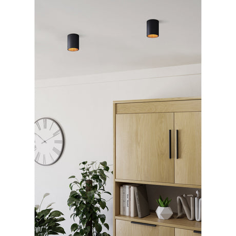 Basmorne LED Flush Ceiling Light in black with a copper-coloured interior, shown as two small cylindrical downlights on a white ceiling above a wooden cabinet and wall clock.