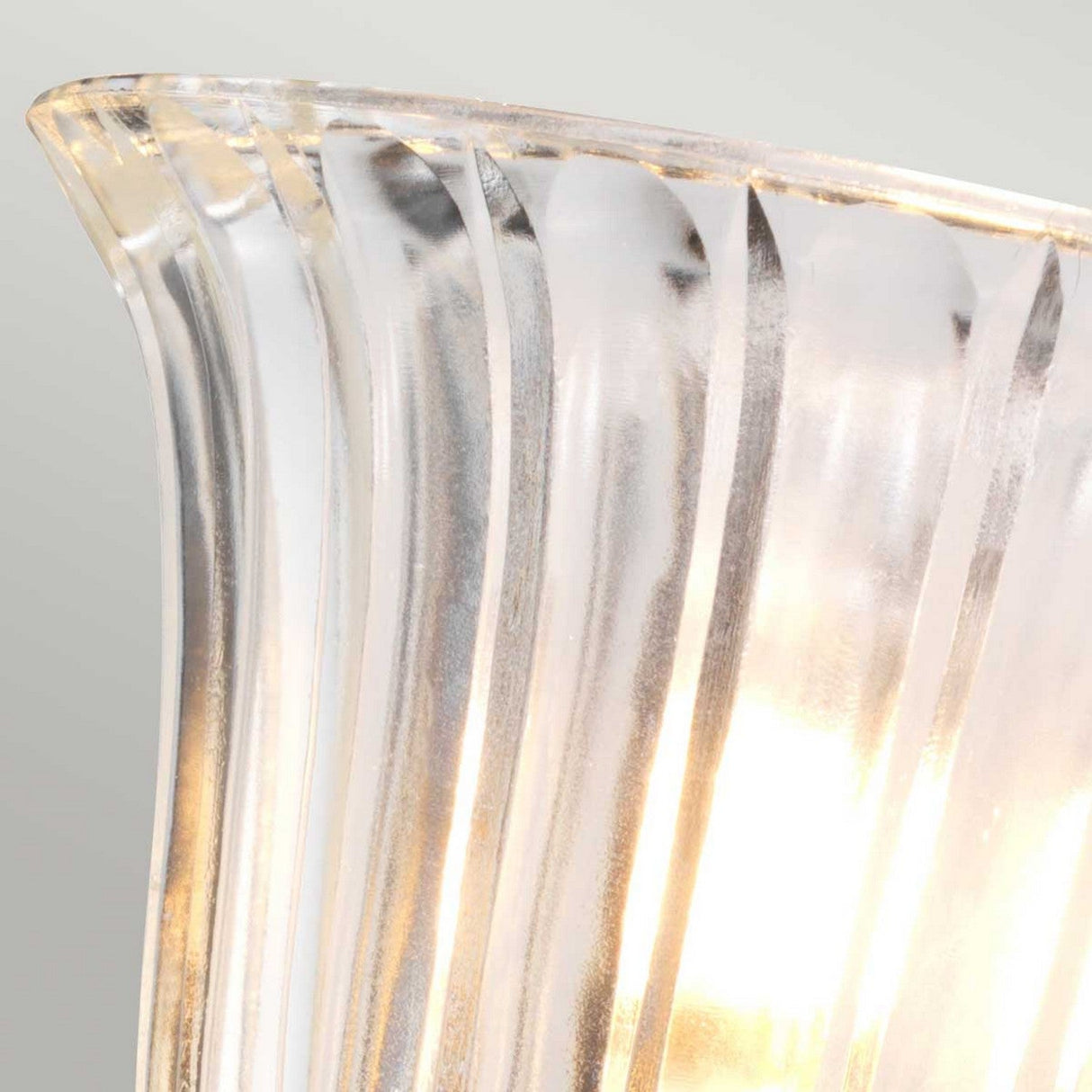 Close-up of a translucent, fluted glass lamp shade with light glowing through it, mounted on the Austen Wall Light - Polished Brass. The piece displays elegant vertical lines and a soft gradient of light to dark tones, adding an air of sophistication to the polished brass fixture.