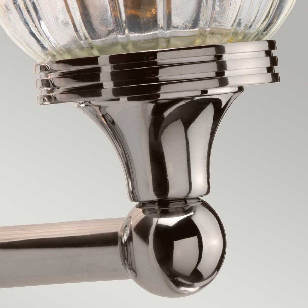 Close-up of the Austen Wall Light sconce in a polished nickel finish. This fixture showcases a timeless design with a ribbed glass shade and a smooth, rounded base that beautifully reflects light. The polished nickel accents add an elegant touch against the soft gradient gray background.