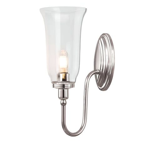 The Blake Wall Light - Polished Nickel showcases a sleek polished nickel base and a gracefully curved arm supporting a clear, flared glass shade. Inside, it houses a light bulb that emits a warm glow, enhancing the modern aesthetic of this wall-mounted sconce.