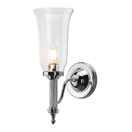 The Carroll-2 Wall Light in polished chrome is a wall-mounted sconce featuring a glass shade. This contemporary lighting fixture includes an elongated stem with a lit bulb inside the transparent shade, highlighting a classic and elegant design. It serves as an IP44 rated wall light, combining style and functionality perfectly.