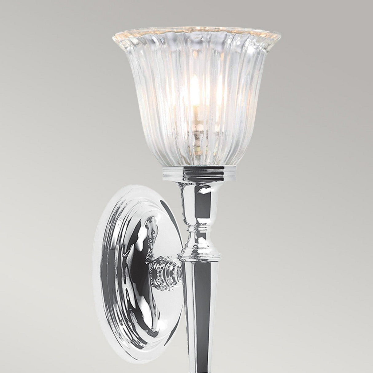The Dryden-1 Wall Light in polished chrome provides a gentle illumination with its ribbed glass lampshade. Designed with elegance and a classic style, it features a round base and a sleek arm that supports the clear, fluted shade. This wall-mounted sconce is compatible with an LED G9 lamp.