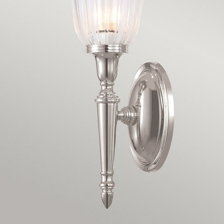 Introducing the Dryden-1 Wall Light - Polished Nickel: This stylish wall sconce showcases a sleek design with a ribbed glass shade set against a plain backdrop. Its elegant, elongated form is enhanced with decorative detailing on the arm and base of the fixture. Compatible with an LED G9 lamp for energy-efficient lighting, it is ideal for modern interiors.