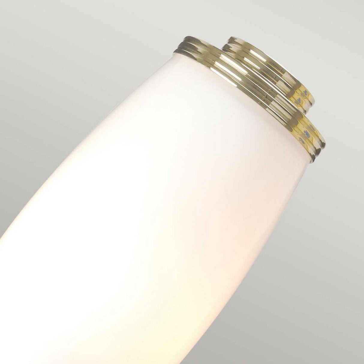 Close-up of the Eliot 2 Light Wall Light in polished brass, featuring a sleek, modern design with a soft white glow, set against a light gray background.