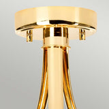 A close-up of the Falmouth 3 Light Semi Flush fixture in French Gold, showcasing polished, curved rods extending from its circular base. The metal surface beautifully reflects light with shiny elegance, highlighting the LED lighting technology. A soft gradient of gray complements this sophisticated design as the background.