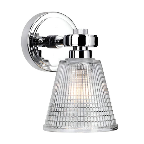 Introducing the Gunnislake 1 Light Wall Light - Polished Chrome, a wall-mounted lamp with a conical prismatic glass shade that features a textured grid-like pattern for casting a cozy warm glow. Its polished chrome base is shiny and round, showcasing a modern design that enhances its sleek aesthetic.