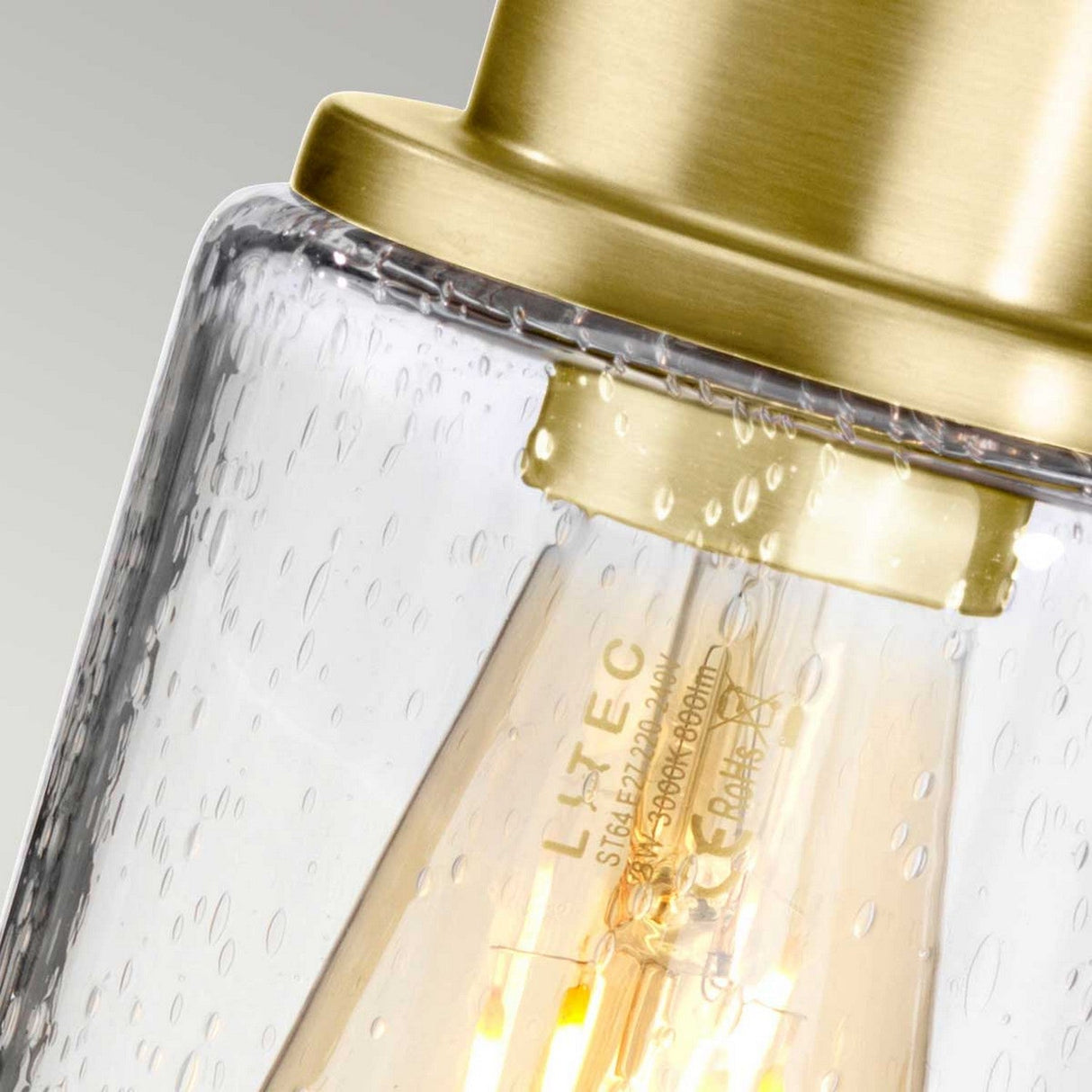 Detailed view of the Morvah 1 Light Outdoor Wall Light in brushed brass, featuring a gold-toned metal and glass design. The pendant includes a textured glass bulb cover with visible imprints, housing an LED bulb that emits a warm glow, offering vintage-inspired lighting charm.