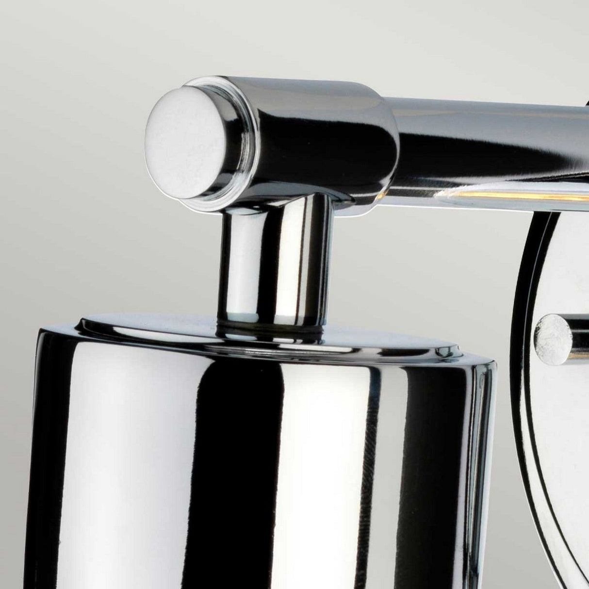 A close-up of the modern Morvah 1 Light Outdoor Wall Light showcases its cylindrical base and horizontal arm. Its polished chrome finish elegantly reflects light against a neutral background, perfectly suited for both indoor and outdoor environments.