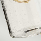 A close-up shot captures a clear glass cup tilted sideways, where tiny bubbles give it a textured look akin to a polished chrome finish. The soft gray background emphasizes the transparency and intricacies of the glass, mirroring the elegant design of the Morvah 1 Light Outdoor Wall Light in Polished Chrome.