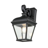 The Bayview 1 Light Outdoor Medium Wall Lantern - Black features a timeless design with a clear glass enclosure that showcases the visible bulb inside. Its graceful curves and traditional style create a striking piece of outdoor lighting.