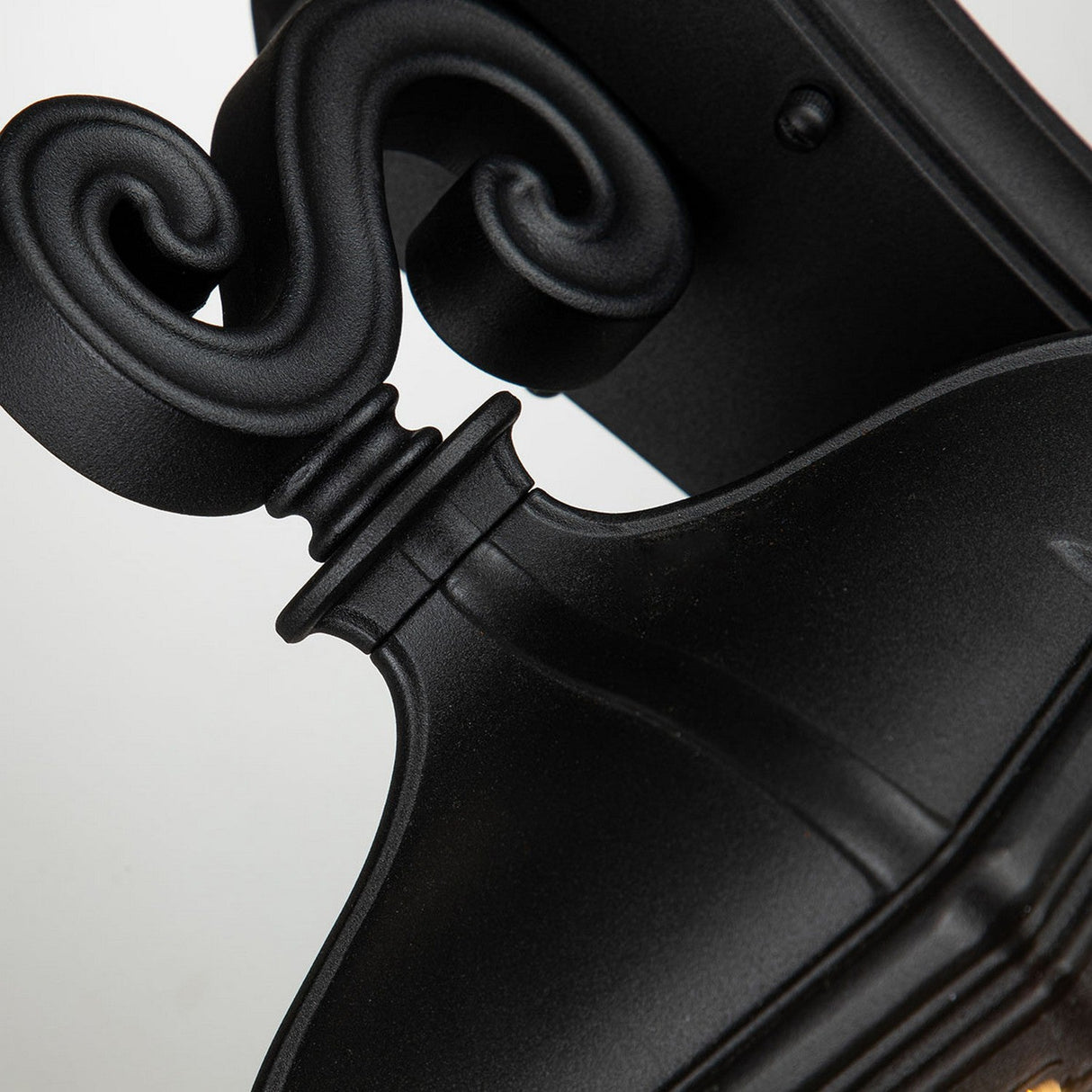 Close-up of a decorative black scroll wall sconce, showcasing an elegant, curled design and sleek finish. The ornamental scroll section resembles the Bayview 1 Light Outdoor Medium Wall Lantern - Black, adding timeless charm to any outdoor lighting setup.