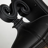 Close-up of a decorative black scroll wall sconce, showcasing an elegant, curled design and sleek finish. The ornamental scroll section resembles the Bayview 1 Light Outdoor Medium Wall Lantern - Black, adding timeless charm to any outdoor lighting setup.