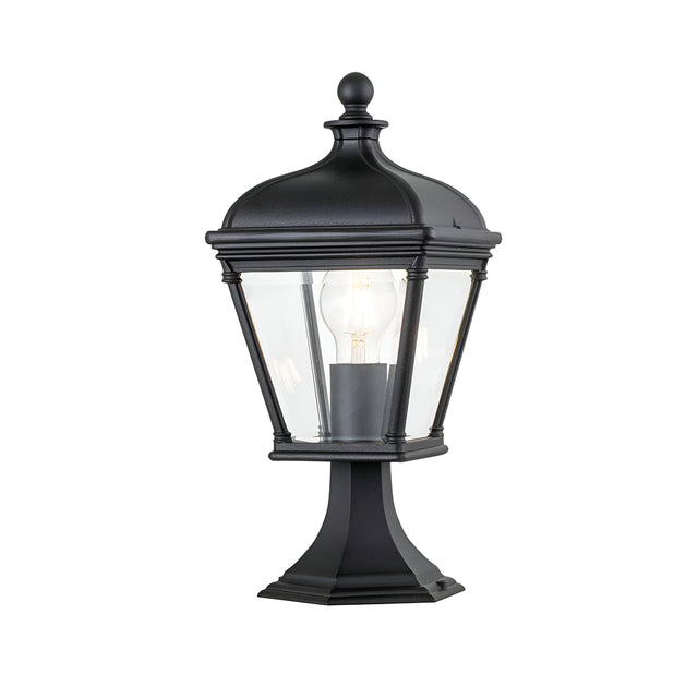 The Bayview 1 Light Medium Pedestal Lantern - Black is a vintage-style outdoor lighting fixture with a clear glass enclosure showcasing a visible light bulb, elegantly mounted on a decorative base. Its classical Georgian design brings timeless charm to any exterior space.