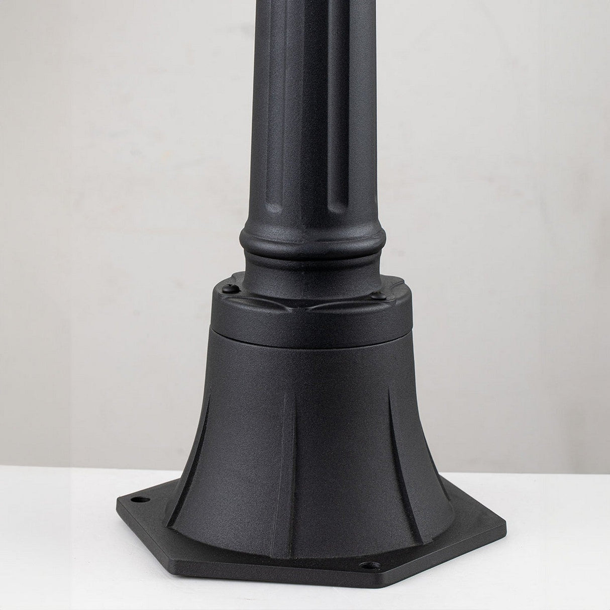 The Bayview 1 Light Medium Pillar Lantern in black showcases Georgian-inspired elegance with its robust, flared design and smooth finish. It is mounted on a flat white surface against a light gray background, making it ideal for sophisticated outdoor lighting.