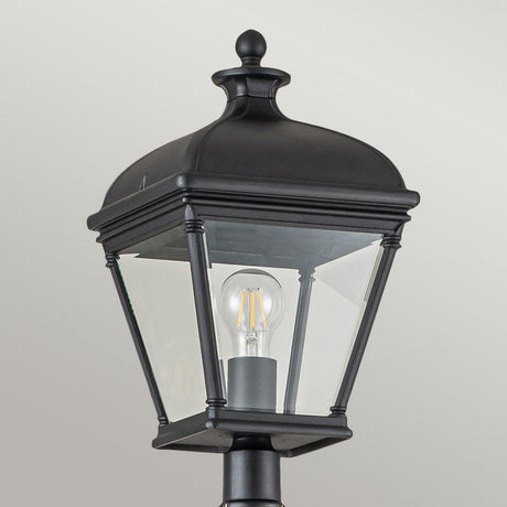 The Bayview 1 Light Lamp Post - Black, ideal for outdoor lighting, features clear glass panels and a visible LED bulb. It showcases a square design with a decorative finial on top, all set against a plain gray background.