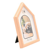 Dog house-shaped photo frame in light brown wood-grain plastic with pitched roof, silver paw print emblem, and white arched mount, shown on a plain white background with a sample dog photo.