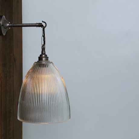 Belvaro Ribbed Glass Wall Light with a bell-shaped clear ribbed shade hung by chain from a hooked arm and round wall plate in antique silver finish, against a plain light background.
