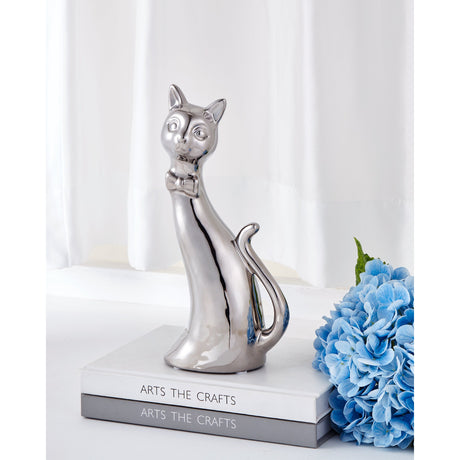 Benangin ceramic cat ornament in mirror-like silver finish, sitting upright with curled tail and bow tie, displayed on stacked books beside blue hydrangea flowers.