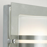 Close-up of the Bern Outdoor 1 Light Wall Lantern in stainless steel with a contemporary brushed metal finish. This fixture showcases a rectangular frosted glass panel, partially framed by metal bands, emanating a soft, warm light.