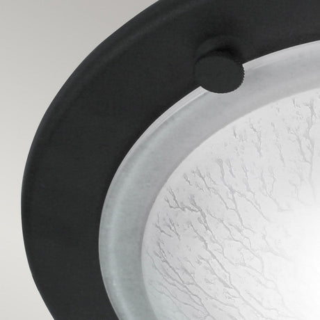 A close-up of the Berwick Flush Light - Black, a contemporary ceiling fixture ideal for modern interiors. It showcases a round frosted glass center surrounded by a sleek black metal rim. The glass features subtle textured patterns, enhanced by a small, round knob for an elegant touch.