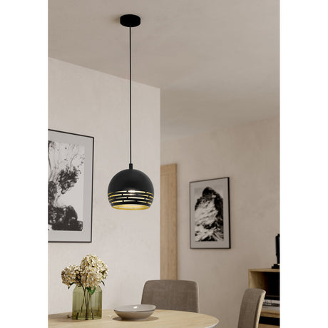 Besmena Pendant Light in black steel with gold interior, dome shade featuring horizontal slots, hung on a black cord above a dining table in a living space.