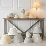 Endon Bevdon 25cm tapered lamp shade in ivory silk with pinch pleats, displayed among a collection of pleated shades on and around a grey console table.