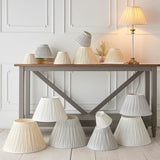 Endon Bevdon tapered lamp shades in ivory silk with pinch-pleat detail, displayed in various sizes on and around a grey console table.