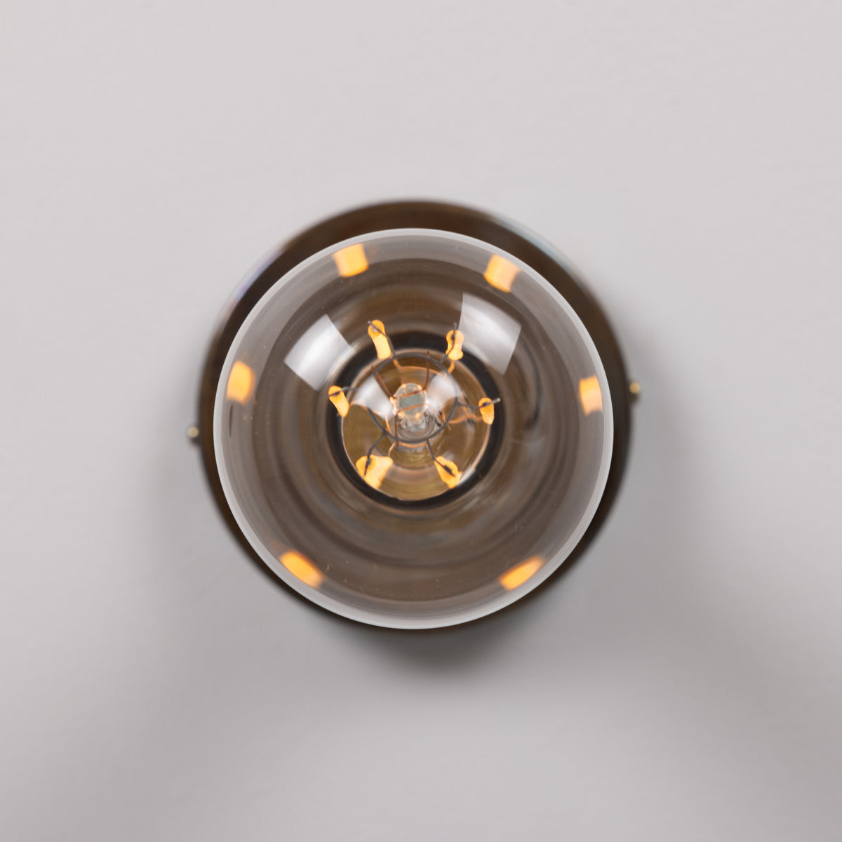 Bexter Vintage Brass Flush Ceiling Light shown close-up with round smoked glass diffuser and exposed E27 bulb, brass fitting against a plain light grey background.