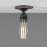 Bexter Vintage Brass Flush Ceiling Light with round ceiling plate and single knurled lampholder holding an exposed bulb, shown against a plain grey background.