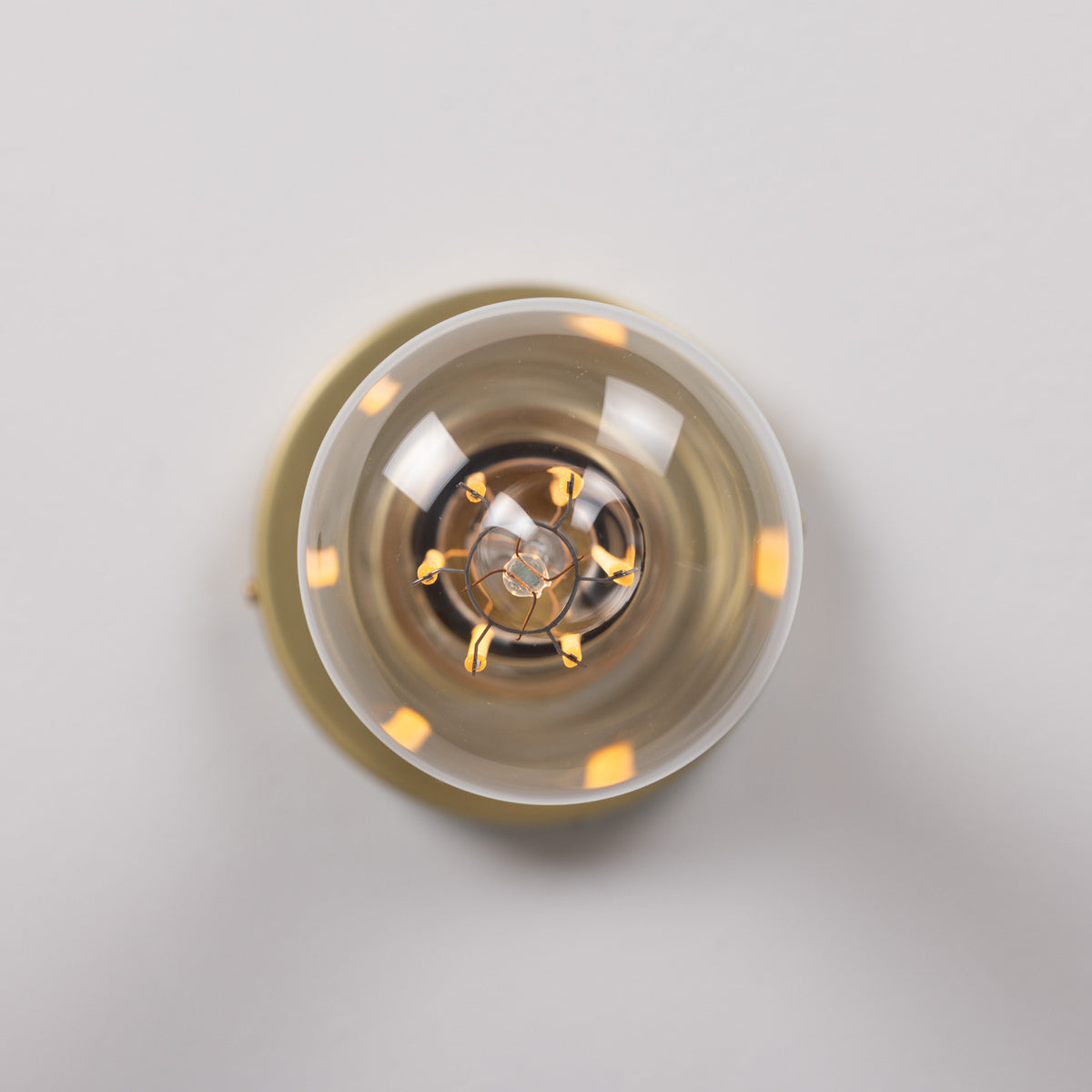Close-up top-down view of the Bexter Vintage Brass Flush Ceiling Light's round glass diffuser revealing an E27 bulb and brass holder, set against a plain light grey background.