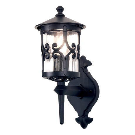 The Hereford 1 Light Outdoor Wall Lantern in black showcases an elegant lantern-style design with a black metal frame and intricate scrollwork. It features a cylindrical glass enclosure, a decorative backplate, and is crafted from durable die-cast aluminum, all expertly mounted on a wall bracket.