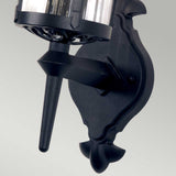 Close-up of the Hereford 1 Light Outdoor Wall Lantern in black, featuring a decorative base and cylindrical glass covering. This wall-mounted light is crafted from die-cast aluminum and is displayed against a plain light-gray background.