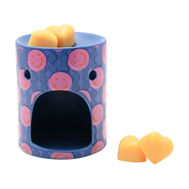 Round ceramic wax melt burner in blue with pink smiley face pattern, arched tealight opening, topped with peach heart-shaped wax melts on a white background.